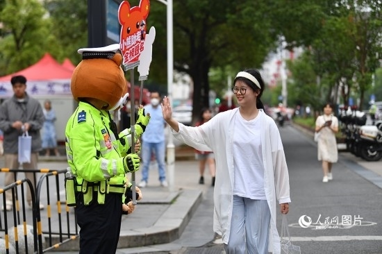 6月7日上午9時(shí)，隨著鈴聲的響起，2023年江西高考正式開考，江西省的53.57萬考生以縣（區(qū)）為單位隨機(jī)安排在全省256個(gè)考點(diǎn)、18968個(gè)考場參加高考。圖為“小熊交警”和考生擊掌鼓勵。 人民網(wǎng)記者 時(shí)雨攝