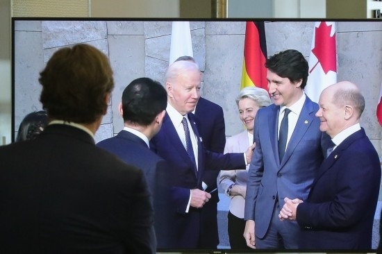 2022年3月24日，在比利時(shí)布魯塞爾的北約總部，一名男子觀看屏幕上美國(guó)總統(tǒng)拜登（右四）、歐盟委員會(huì)主席馮德萊恩（右三）、加拿大總理特魯多（右二）、德國(guó)總理朔爾茨（右一）出席七國(guó)集團(tuán)峰會(huì)合影儀式的畫面。新華社記者鄭煥松攝