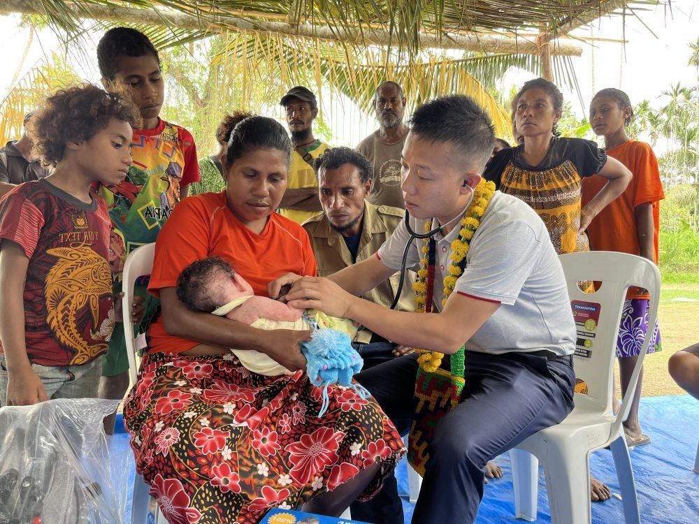 2023年8月5日，在巴布亞新幾內(nèi)亞中央省的一個(gè)村莊里，第12批援巴新中國醫(yī)療隊(duì)副隊(duì)長、新生兒科副主任醫(yī)師劉振球?yàn)閶雰禾仿犜\檢查。泰樂出生時(shí)患有重癥，一度生命垂危，經(jīng)過劉振球與當(dāng)?shù)蒯t(yī)護(hù)人員的救治最終痊愈。從2002年起，中國連續(xù)向巴新派出12批醫(yī)療隊(duì)，為提高巴新醫(yī)療衛(wèi)生水平作出積極貢獻(xiàn)。