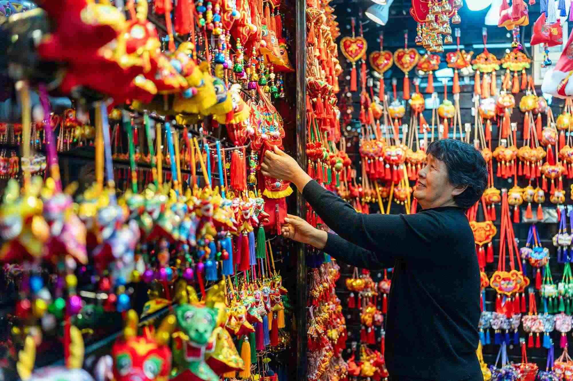 2023年12月11日，金華義烏國(guó)際商貿(mào)城，龍年喜慶用品掛滿(mǎn)攤位，顧客正在挑選中。