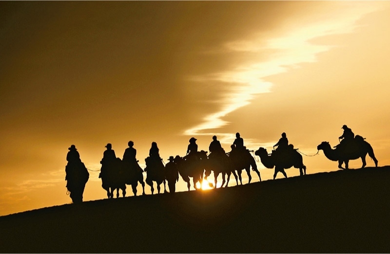 新時(shí)代以來(lái)，文化和旅游深度融合發(fā)展體制機(jī)制不斷健全，成功走出了一條獨(dú)具特色的中國(guó)旅游發(fā)展之路。圖為2024年9月1日清晨，游客在甘肅省敦煌市鳴沙山月牙泉景區(qū)乘騎駱駝，欣賞大漠風(fēng)光，體驗(yàn)絲路風(fēng)情。 新華社發(fā) 張曉亮/攝