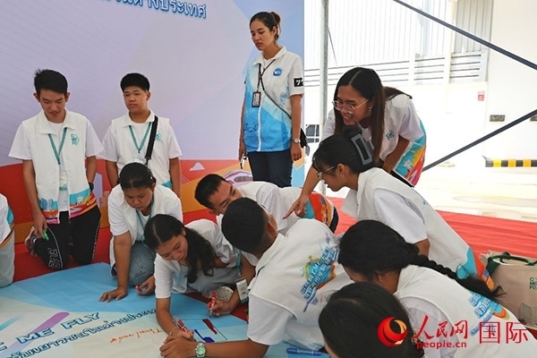 泰國學(xué)生在開營儀式展板上繪制圖案。人民網(wǎng)記者 白元琪攝