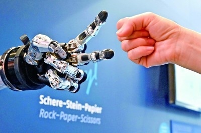 在德國漢諾威工博會上，參觀者與一款智能機器人進行“石頭剪子布”游戲。新華社發(fā)